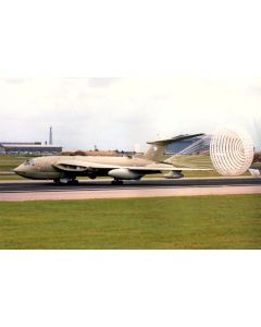 Avro Vulcan bomber aircraft landing with a deployed parachute on a runway, set against a grassy field and hangars in the background.