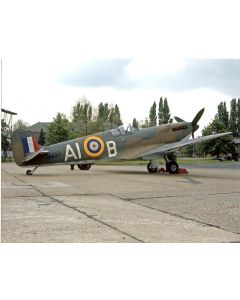 World War II-era Supermarine Spitfire aircraft parked on a tarmac, featuring British roundel and markings, surrounded by trees and cloudy sky.