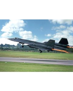 Sleek black aircraft taking off with afterburners engaged, set against a bright blue sky and green landscape.