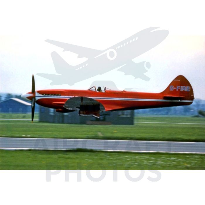 Red vintage aircraft with registration G-FIRE taking off on a runway, showcasing its unique design against a grassy landscape.