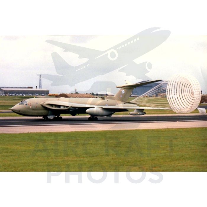Avro Vulcan bomber aircraft landing with a deployed parachute on a runway, set against a grassy field and hangars in the background.