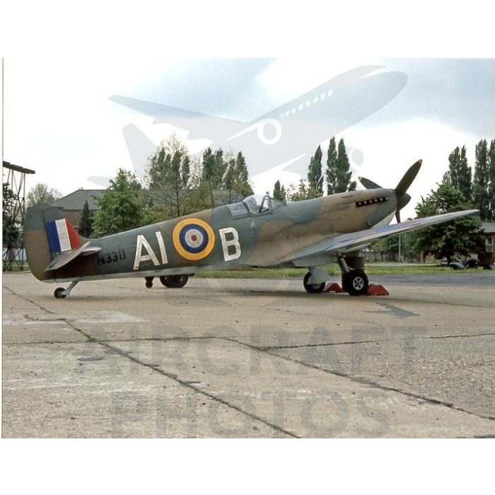 World War II-era Supermarine Spitfire aircraft parked on a tarmac, featuring British roundel and markings, surrounded by trees and cloudy sky.