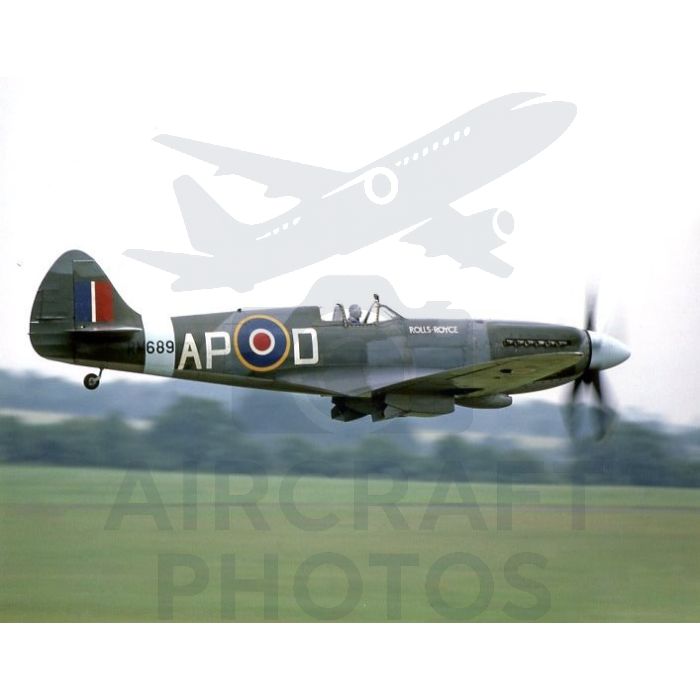 A vintage military aircraft, a Supermarine Spitfire, flying over a green landscape, featuring a dark green body with distinctive roundel markings and "APOD" painted on the side.
