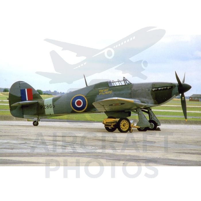 Supermarine Spitfire PZ865 on the tarmac, showcasing its distinctive green and grey camouflage with a roundel and "The Last of the Many!" inscription.
