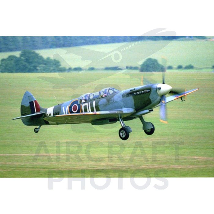 Vintage Supermarine Spitfire aircraft flying low over a green landscape.